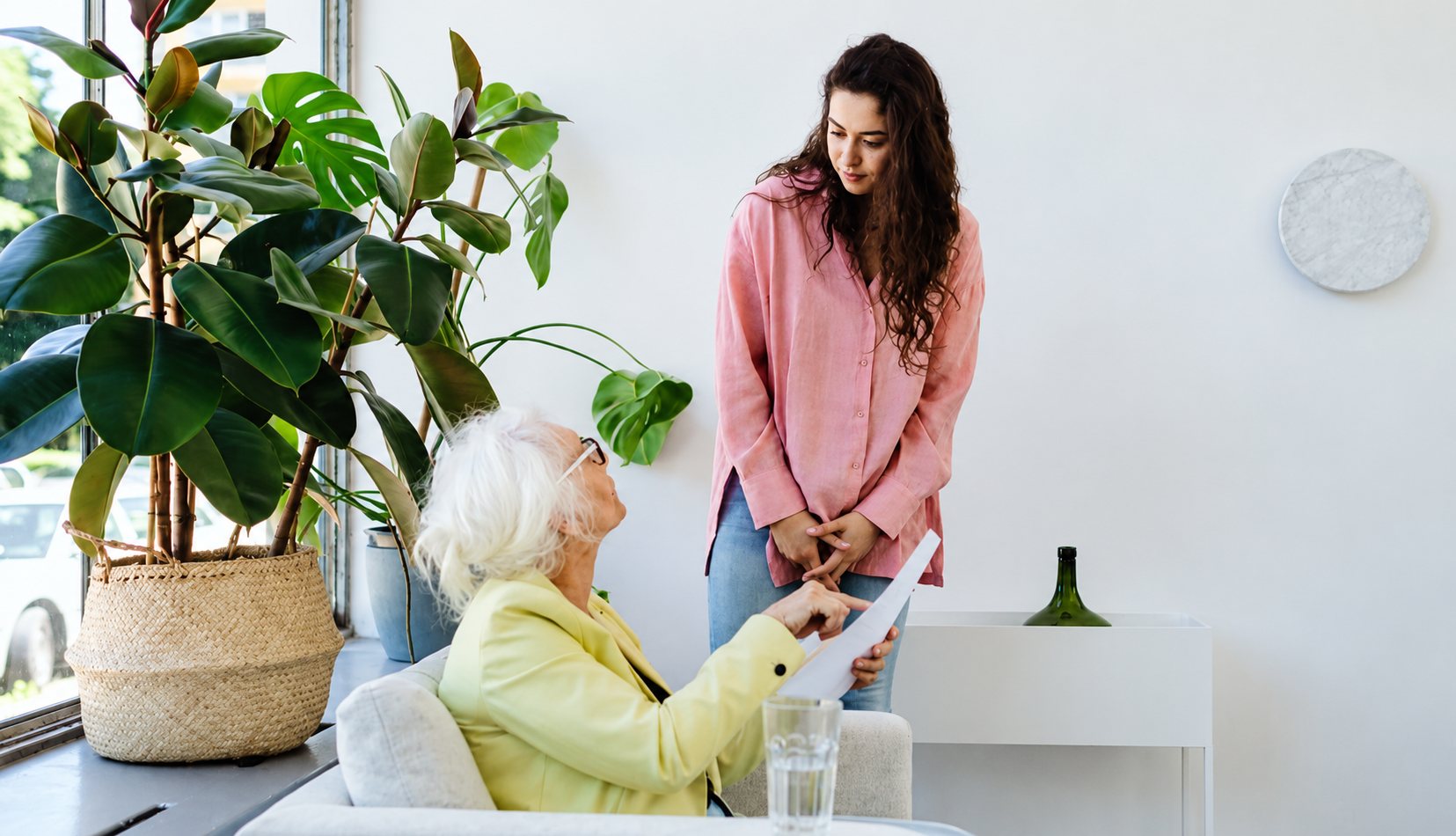 Une femme debout parle à une femme âgée assise près d’une plante.