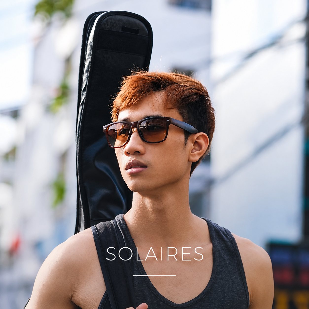 Un jeune homme en lunettes de soleil, une housse de guitare sur le dos, en ville.